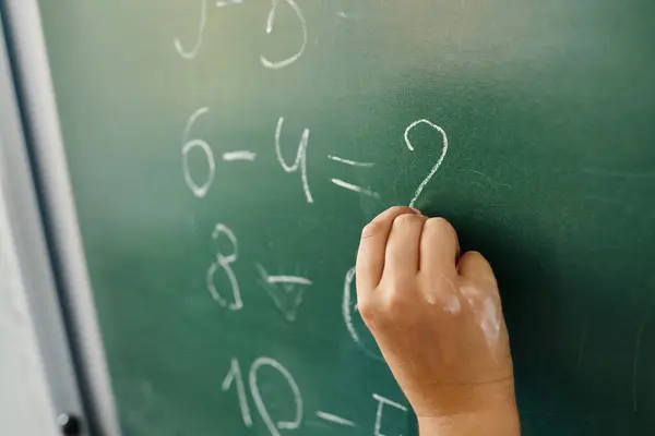 Kid writes on a blackboard with white chalk in lively classroom setting, math — Stock Photo