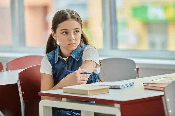A young girl sits at a table engrossed in a book, absorbing knowledge in a bright, lively classroom setting. — Stock Photo
