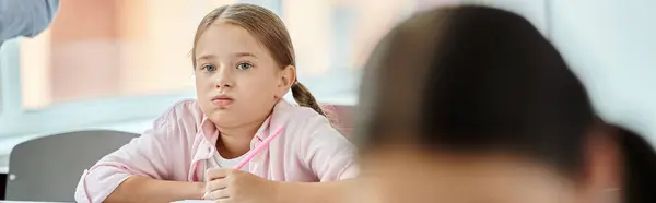 Молода дівчина сидить за столом, захоплений своїм завданням, з нудним виразом обличчя в класі. — стокове фото