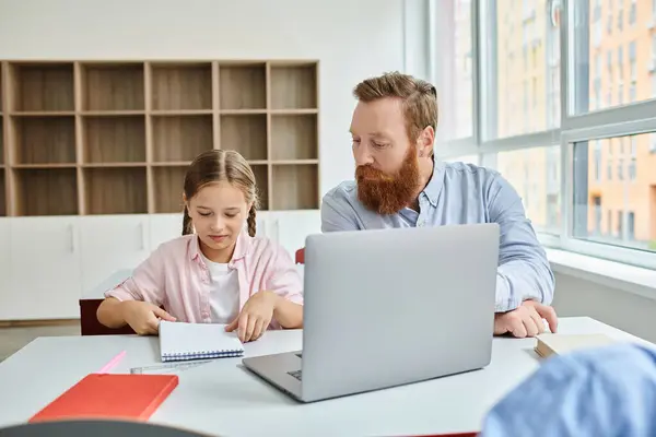 A man and a little girl sit attentively in front of a laptop, engaging in educational content during a lively classroom session. — Stock Photo