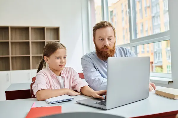 Un uomo e una bambina seduti di fronte a un computer portatile, assorti in un'attività di apprendimento. L'uomo sembra insegnare e guidare la ragazza mentre ascolta attentamente. — Foto stock