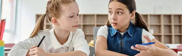 Two girls with pens in hand, focused and engaged in a creative task at a brightly lit classroom table. — Stock Photo