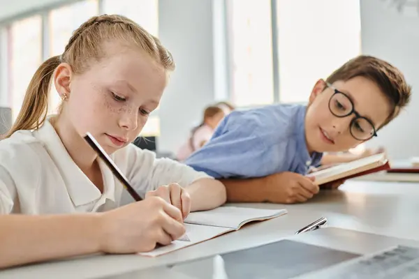 A young girl and boy deep in thought as they tackle their homework in a lively classroom. — Stock Photo