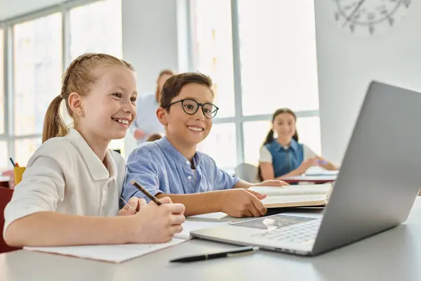 Группа детей, сидящих за столом, сосредоточенных на ноутбуке в ярком классе. — стоковое фото