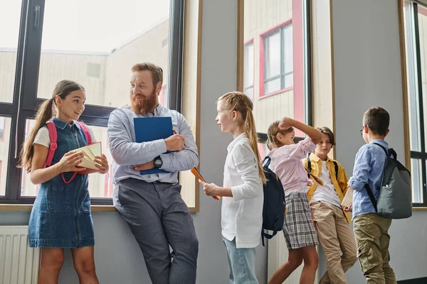 A group of young people standing in unity, listening to their male teacher in a bright, lively classroom setting. — Stock Photo