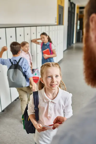 Children eagerly check lockers in a lively hallway, guided by a male teacher in a bright classroom setting. — Stock Photo