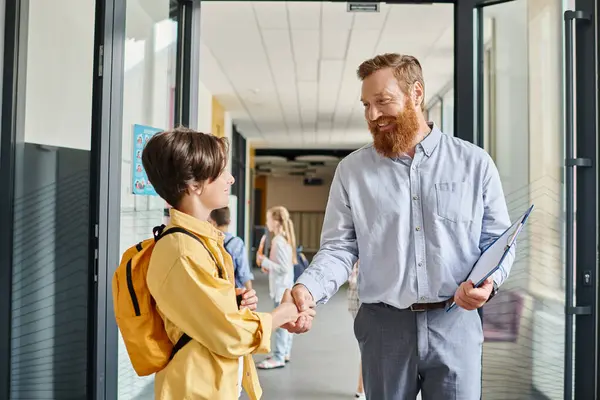 Un hombre en un salón de clases, estrechando la mano de un niño, simbolizando una interacción significativa y positiva entre las diferentes generaciones. - foto de stock