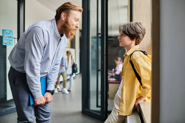 A man stands next to a little boy in a bright classroom, offering guidance and instruction. — Stock Photo