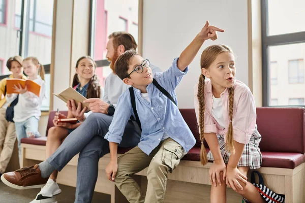 Un gruppo di bambini si siede con attenzione su una panchina mentre un insegnante di sesso maschile li istruisce in un ambiente di classe luminoso e vivace. — Foto stock
