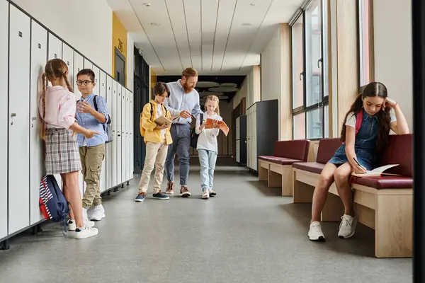 Un gruppo di individui, tra cui un insegnante uomo, in piedi in un corridoio da armadietti, impegnati in conversazione e istruzione. — Foto stock