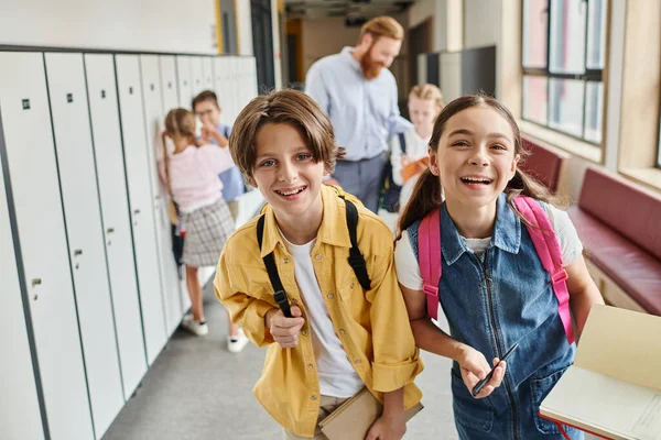 Разнообразная группа детей идет по школьному коридору, заполненному красочными шкафчиками, болтая и смеясь, когда они направляются в следующий класс. — стоковое фото