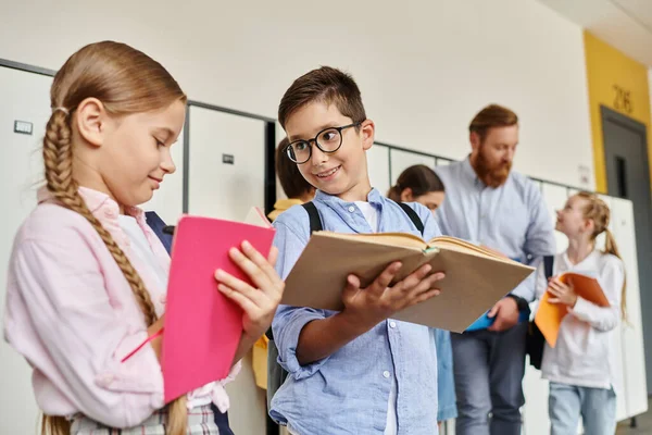 A group of children stand next to each other in a bright, lively classroom, while their teacher watches on. — Stock Photo
