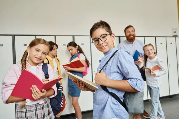 Un grupo diverso de niños, guiados por su maestro masculino, están atentos en un pasillo luminoso, listos para embarcarse en una nueva aventura de aprendizaje. - foto de stock