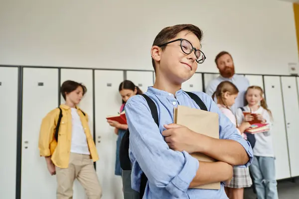 A young boy stands in front of a row of lockers, engrossed in a book he holds in his hands while in a school hallway. — Stock Photo