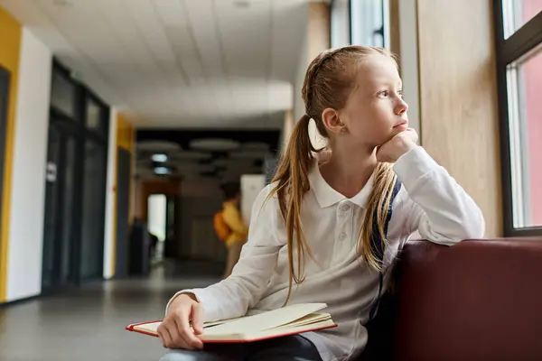 A young girl with long dark hair sits alone on a wooden bench, engrossed in a book, deep in thought. — Stock Photo