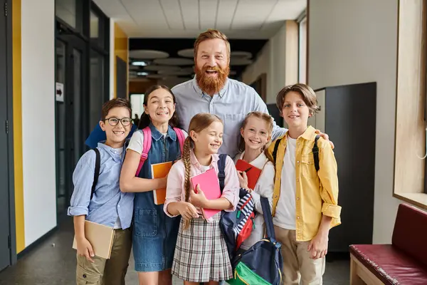 Un insegnante dedicato si trova tra un gruppo multiculturale di bambini in un vivace corridoio scolastico, coinvolgendoli in una sessione di apprendimento interattiva.. — Foto stock