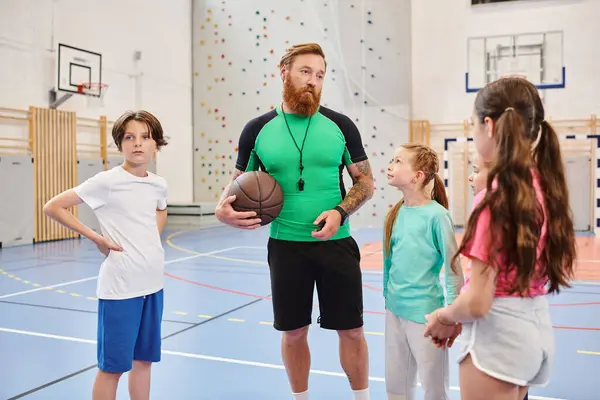 Un hombre sosteniendo una pelota de baloncesto se para en una cancha de baloncesto, listo para un partido o sesión de práctica. - foto de stock