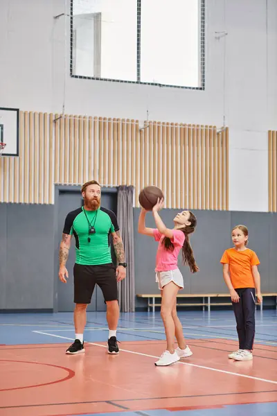 Un hombre, mostrando técnicas de baloncesto, juega con niños en un gimnasio lleno de energía y emoción. - foto de stock