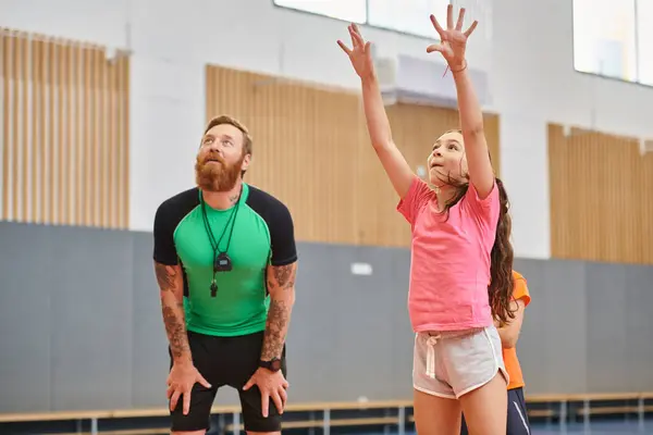 Un hombre y una niña jugando al baloncesto enérgicamente en un gimnasio, mostrando trabajo en equipo, habilidad y camaradería. - foto de stock