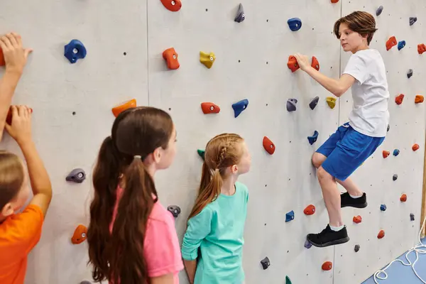 Eine Gruppe kleiner Kinder steht gemeinsam vor einer Kletterwand und hört aufmerksam den Anweisungen ihrer Lehrer zu, bevor sie versuchen, die Wand zu erklimmen.. — Stockfoto