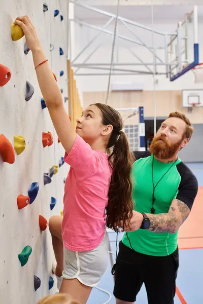 A girl bravely climbing up a towering wall, pushing limits in a thrilling display of teamwork and determination. — Stock Photo