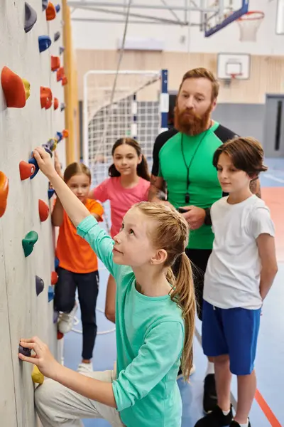 Ein männlicher Lehrer weist eine bunt gemischte Gruppe von Kindern und Erwachsenen ein, während sie an einer Kletterwand stehen und sich auf eine abenteuerliche Kletterherausforderung vorbereiten. Helles, lebendiges Klassenzimmer steigert die Spannung. — Stockfoto