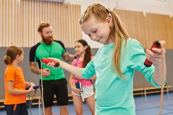 Un gruppo eterogeneo di bambini si impegna in una sessione di ginnastica energica, con una ragazza che tiene con fiducia una corda da salto come l'insegnante maschio li istruisce e li guida.. — Foto stock