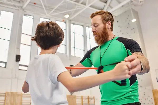 A man peacefully assists a young boy in a vibrant school gym — Stock Photo