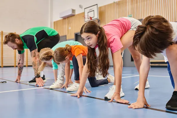 A man teacher stands atop a vibrant blue floor, surrounded by a diverse group of children. The classroom exudes brightness and liveliness. — Stock Photo