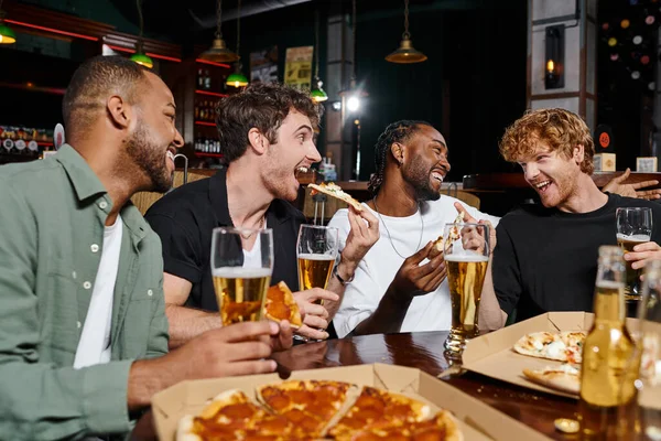 Groupe de quatre amis interraciaux heureux manger de la pizza et boire de la bière dans le bar, les hommes sur enterrement de vie de garçon — Photo de stock