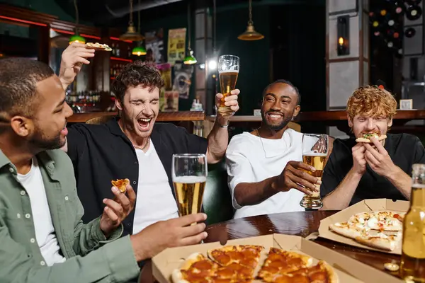 Hombre excitado sosteniendo pizza y cerveza mientras grita cerca de amigos interracial en el bar, amistad masculina - foto de stock