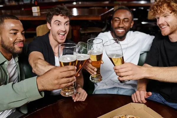 Quatre amis multiculturels excités cliquetis avec des verres de bière dans le bar, les hommes sur enterrement de vie de garçon — Photo de stock
