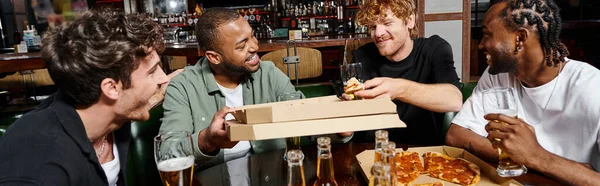 Four happy multiethnic friends sharing pizza and drinking beer in bar, men on bachelor party, banner — Stock Photo