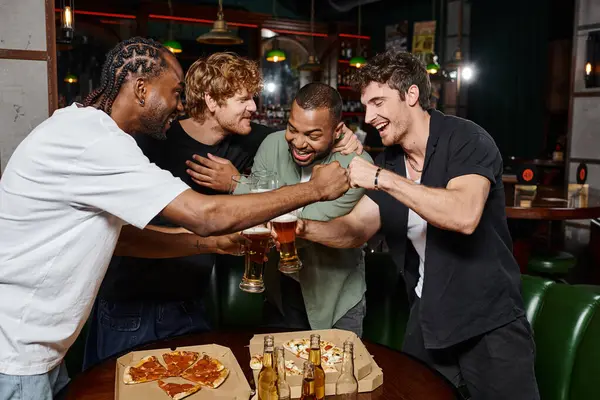 Счастливые межрасовые друзья мужского пола кулаком ударяясь за бокалы пива в баре, мальчишник — стоковое фото