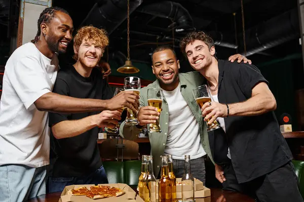 Feliz interracial hombres tostadas con vasos de cerveza en el bar durante la despedida de soltero, amistad masculina - foto de stock
