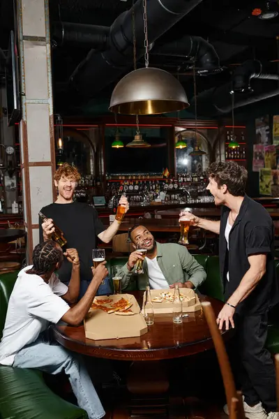 Excited interracial friends toasting with bottles and glasses of beer in bar, spending time together — Stock Photo