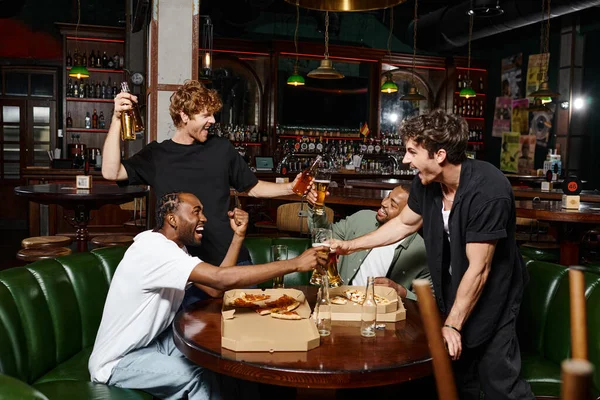 Happy interracial friends toasting with bottles and glasses of beer in bar, spending time together — Stock Photo