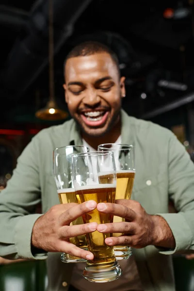 Homme afro-américain joyeux tenant trois verres de bière dans le bar, avoir du plaisir pendant les week-ends — Photo de stock