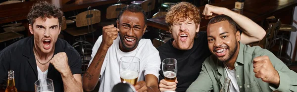 Pancarta, aficionados al fútbol multiétnico emocionados sosteniendo vasos de cerveza y vitoreando, amigos varones en el bar - foto de stock