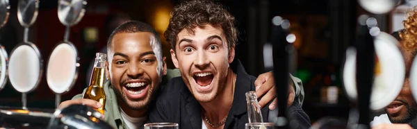 Excited interracial friends hugging and holding beer, spending time in bar, male friendship banner — Stock Photo