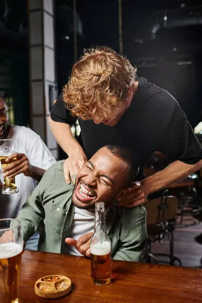 Ruiva homem cócegas feliz Africano americano noivo durante despedida de solteiro no bar, amizade masculina — Fotografia de Stock