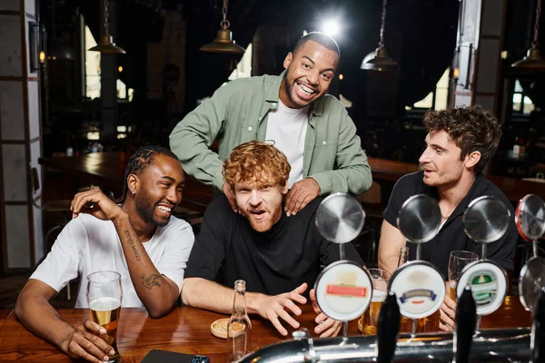 African american man touching shoulders of redhead groom near friends during bachelor party in bar — Stock Photo