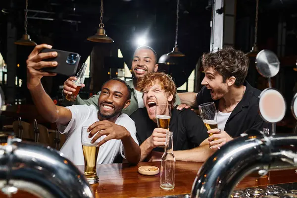 Щасливі мультикультурні чоловіки беруть селфі на смартфон під час пиття пива в барі, холостяцька вечірка — стокове фото