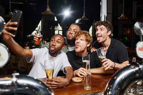 Drôles d'hommes multiculturels prenant selfie sur smartphone tout en collant la langue pendant la fête de célibataire — Photo de stock