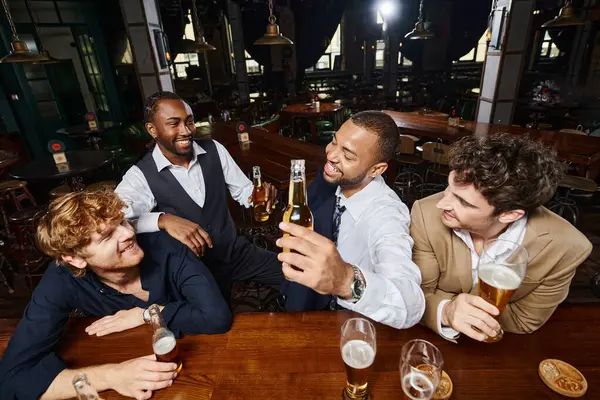 Colegas felices en ropa formal charlando y bebiendo cerveza en el bar, pasar tiempo juntos después del trabajo - foto de stock