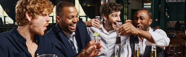 Amigos multiétnicos animado segurando tiros de tequila com limão perto de copos de cerveja no bar, banner — Fotografia de Stock