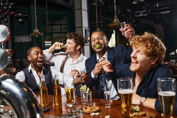 Gruppe von vier fröhlichen und betrunkenen multiethnischen Freunden in formeller Kleidung trinken Tequila in der Bar nach der Arbeit — Stockfoto