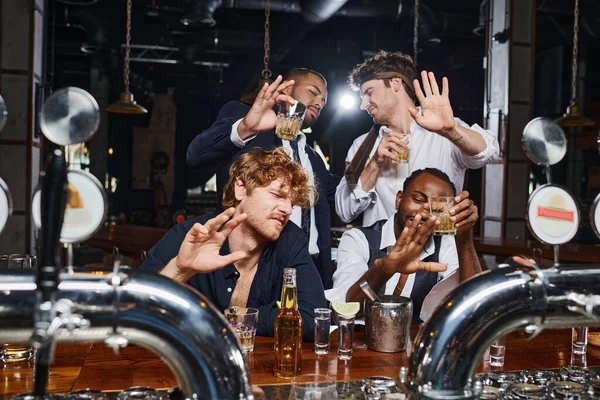 Vier betrunkene multikulturelle Freunde, die Gesichter mit grellem Licht, Tequila-Shots, Bier und Whiskey bedecken — Stockfoto