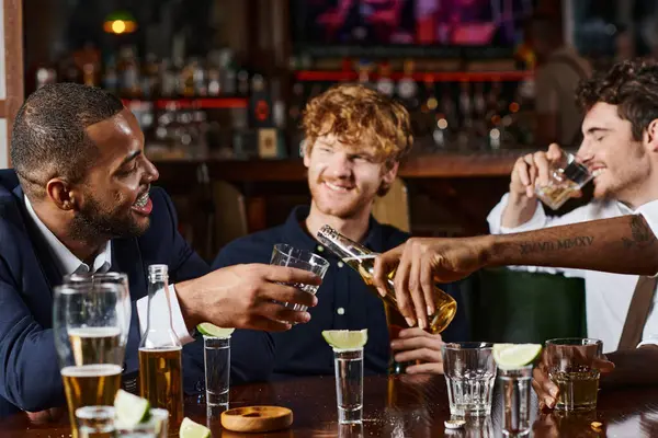 Tatoué afro-américain verser de la bière dans un verre d'ami pendant la fête de célibataire, hommes interracial — Photo de stock