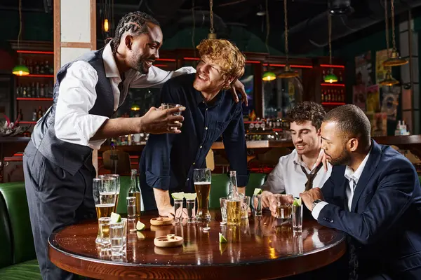 Amigos borrachos interracial abrazar y beber bebidas alcohólicas mientras se relaja después del trabajo en el bar - foto de stock